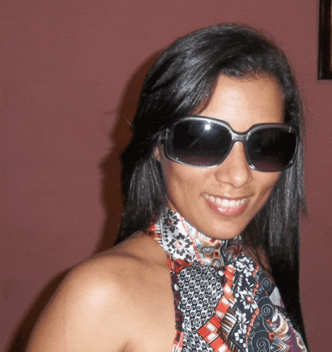 a woman wearing sunglasses and a scarf around her neck smiles