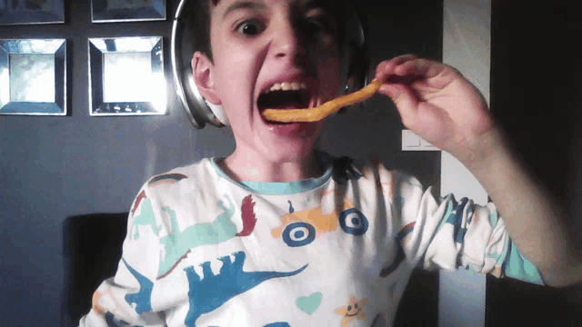 a young boy wearing headphones and a dinosaur shirt is eating a french fry