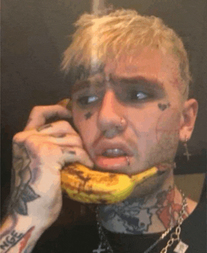 a man with a tattoo on his face is talking on a cell phone while holding a banana in his mouth .