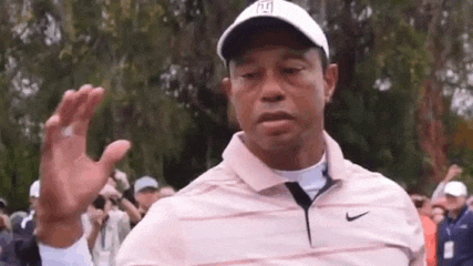 tiger woods is wearing a pink shirt and a white hat while waving at the camera .