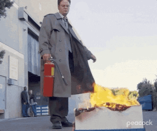 a man in a trench coat is holding a fire extinguisher in front of a burning box that says peacock