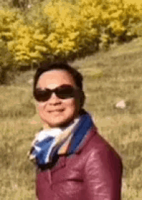 the man is wearing sunglasses and a scarf and is standing in a field .