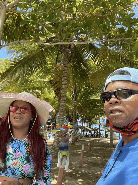 a man and a woman wearing hats and sunglasses stand in front of palm trees