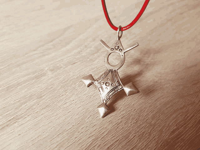 a silver pendant on a red string on a wooden table