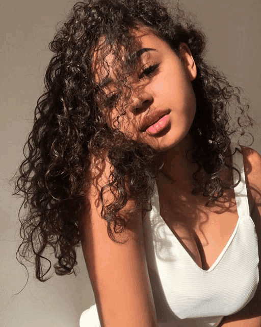 a woman with curly hair is wearing a white top