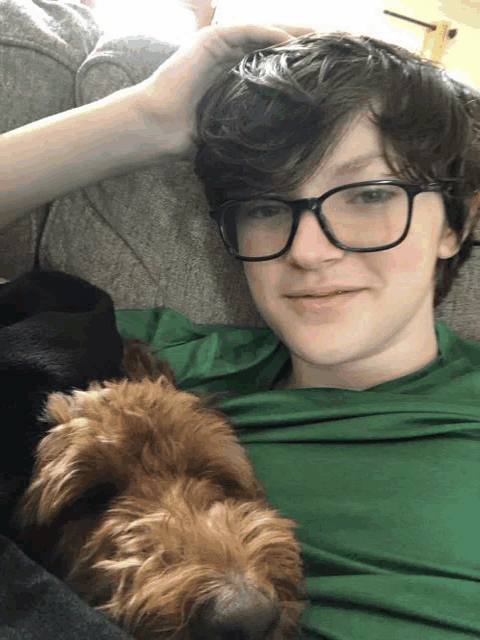 a young man wearing glasses is laying on a couch with a dog