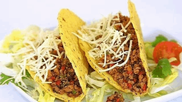 three tacos are sitting on a white plate with lettuce , tomatoes and cheese .