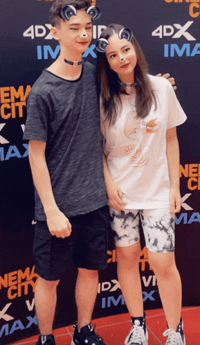 a boy and a girl are posing for a picture in front of a 4dx sign