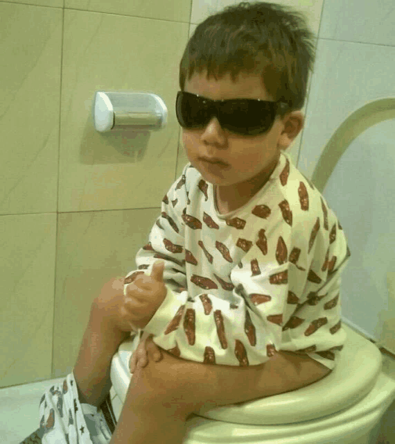 a young boy wearing sunglasses sits on a toilet in a bathroom