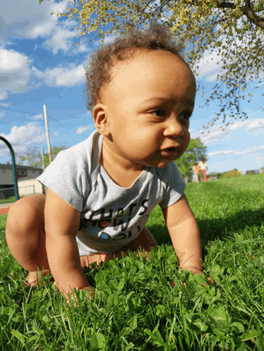 a baby crawling in the grass wearing a shirt that says ' guess ' on it