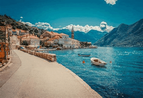 a small town on the shore of a lake with boats and mountains in the background .