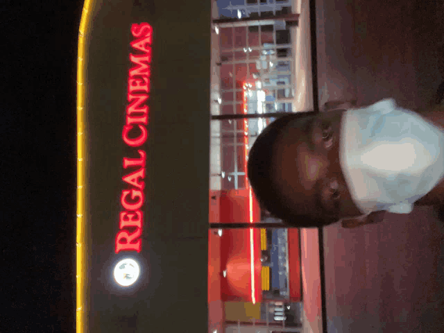 a man wearing a mask stands in front of a sign for regal cinemas