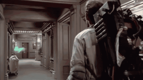 a man is walking down a hallway with a ghost coming out of the door .