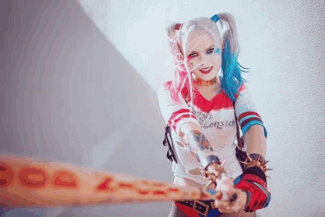 a woman in a harley quinn costume is holding a bat that says suicide squad on it