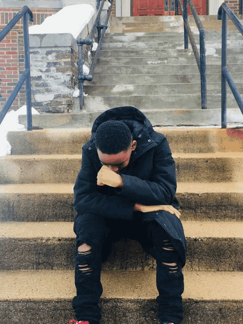 a young man sits on the steps of a building with his head down