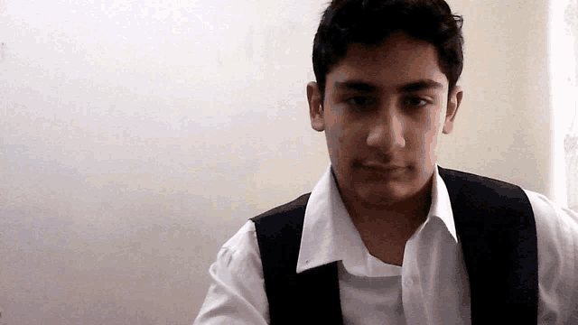 a young man wearing a white shirt and black vest