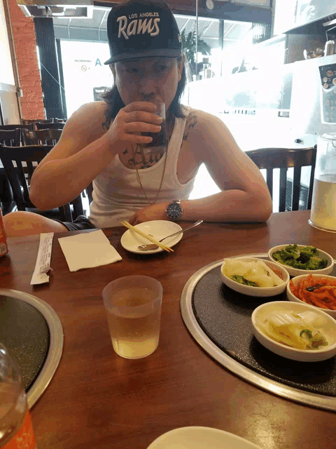 a man wearing a los angeles rams hat sits at a table with food