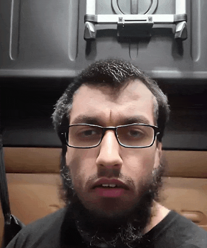 a man with glasses and a beard looks at the camera with his mouth open