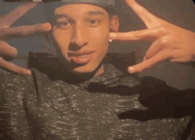 a young man wearing a hat and a grey shirt is making a peace sign