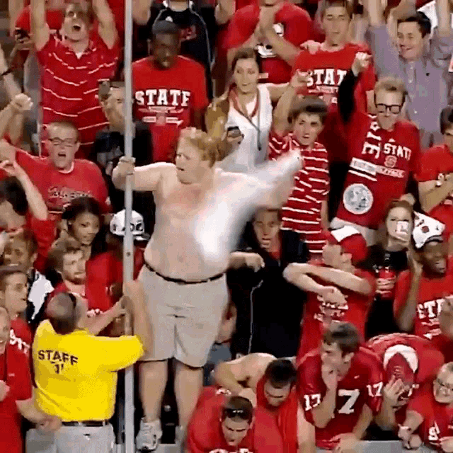 a man in a yellow staff shirt stands in front of a crowd of people wearing red shirts that say state