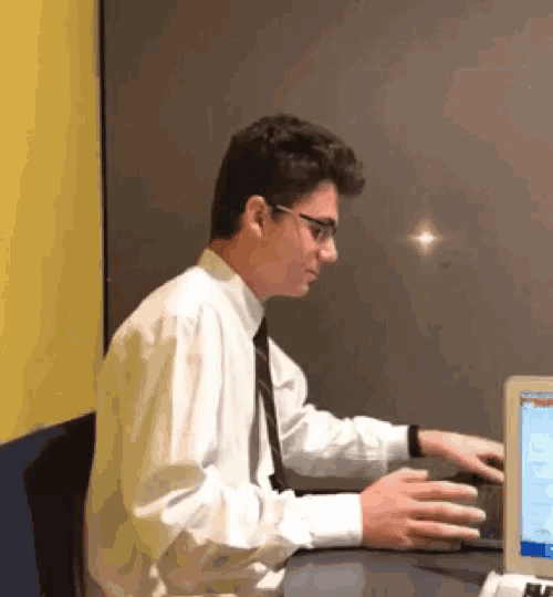 a man in a white shirt and tie is sitting at a desk in front of a computer screen .