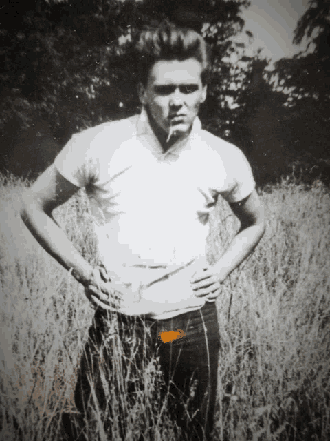 a man standing in a field with his hands on his hips smoking a cigarette