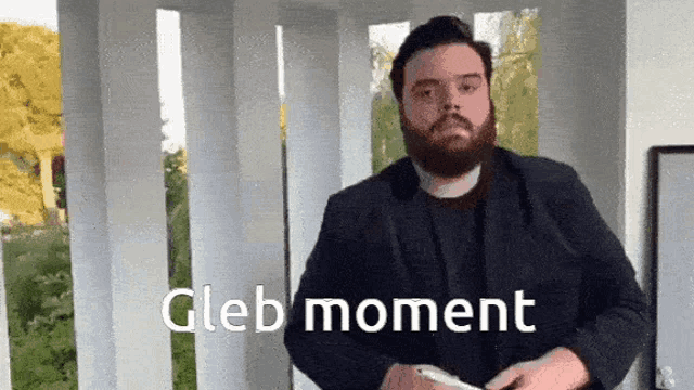 a man with a beard is standing in front of a white wall with the words gleb moment written on it