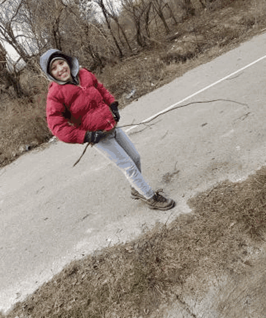 a young boy in a red jacket is standing on the side of the road holding a stick .