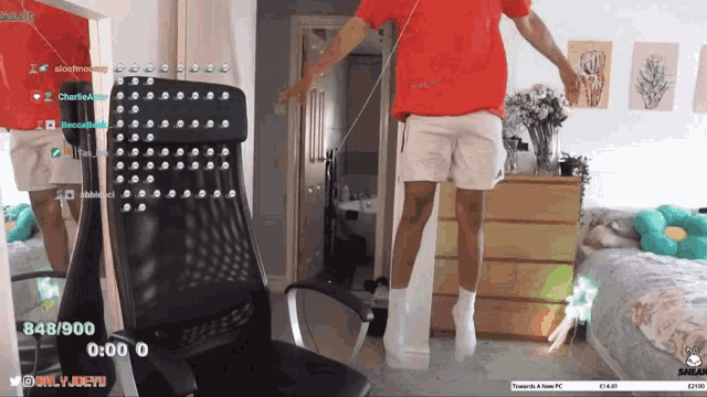 a man in a red shirt is jumping in front of a chair in a bedroom