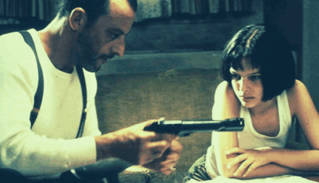 a man is pointing a gun at a woman who is sitting at a table