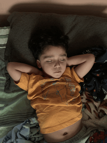 a young boy wearing an orange shirt with a dinosaur on it is sleeping