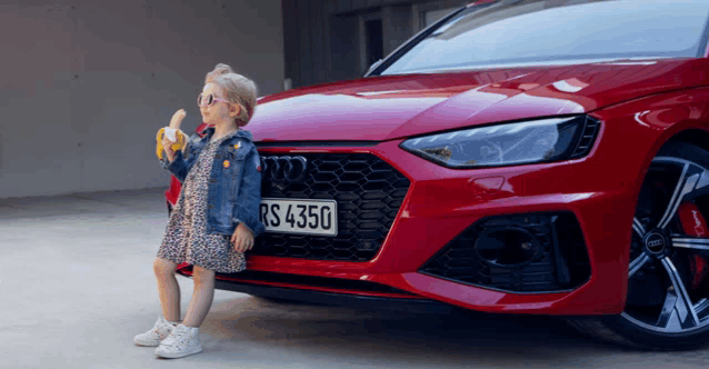 a little girl eating a banana in front of an audi