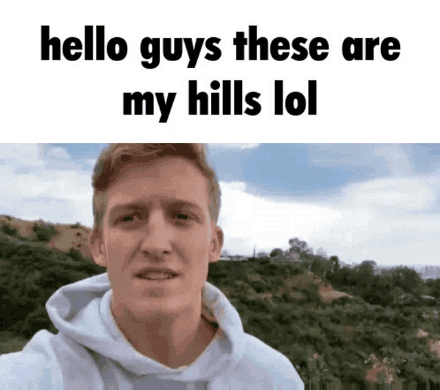 a man in a white hoodie is taking a selfie in front of a mountain .