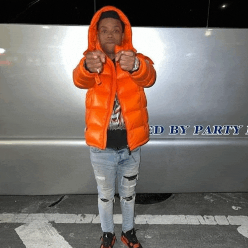 a man in an orange jacket is standing in front of a limousine that says ' ed by party ' on the side .