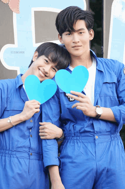 two men in blue jumpsuits hold blue hearts in front of a sign that says " i team sandai "