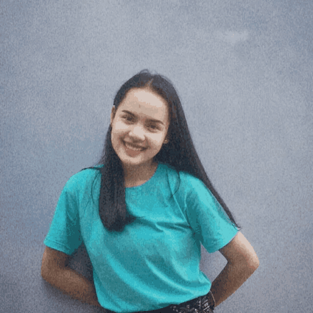 a woman wearing a blue shirt is smiling and standing with her hands on her hips