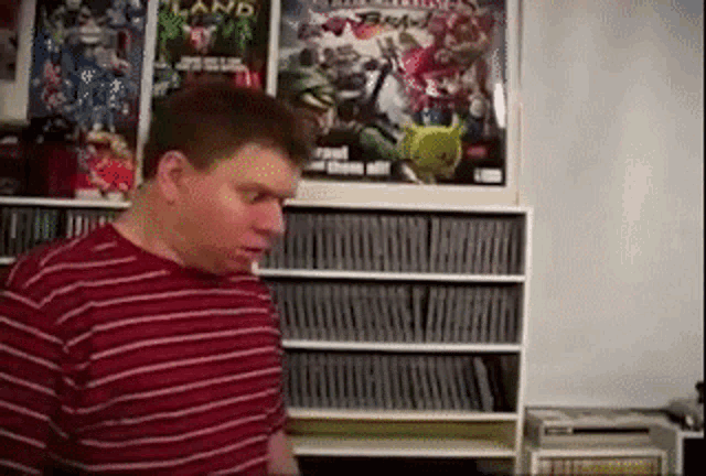 a man in a red and white striped shirt is standing in front of a bookshelf filled with books .