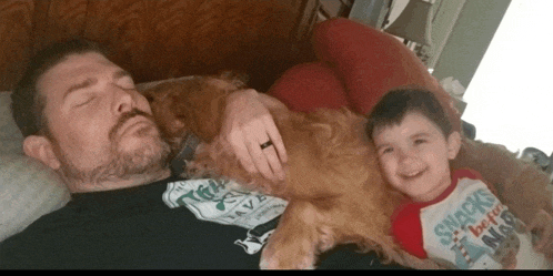 a man laying on a bed with a child and a dog wearing a shirt that says snacks before nap