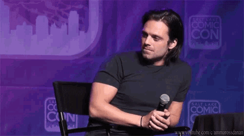 a man is sitting at a table with a microphone in front of a wall that says salt lake comic con .