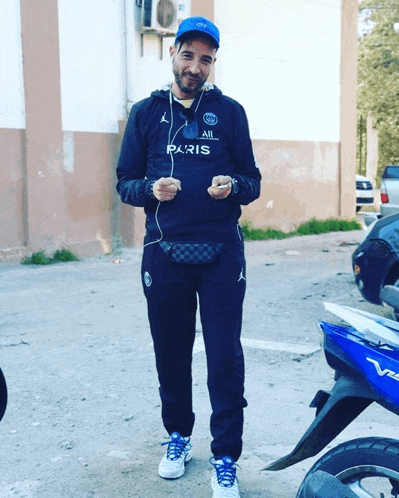 a man wearing a paris shirt is standing in front of a blue motorcycle