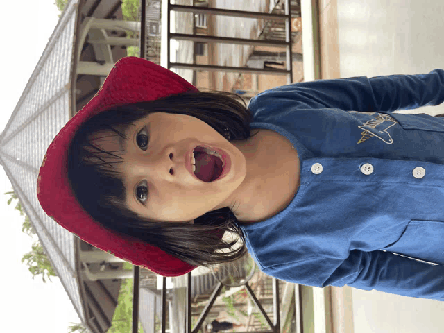 a little girl wearing a red hat and a blue shirt making a funny face