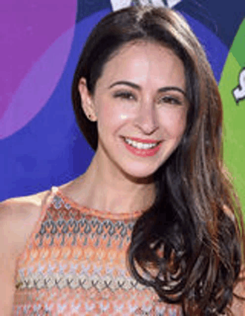 a woman with long hair is smiling for the camera while standing on a red carpet .