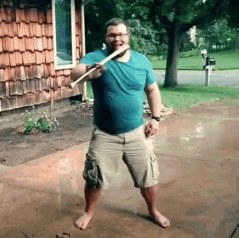 a man in a blue shirt and khaki shorts is holding a wooden stick in front of a house .