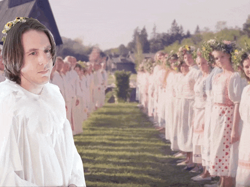 a man in a white shirt stands in front of a row of women with flower crowns on their heads