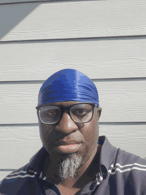 a man wearing glasses and a blue headband stands in front of a white wall