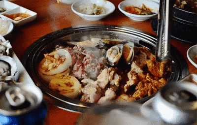 a person is cooking food in a pot on a table with a can of beer in the foreground .