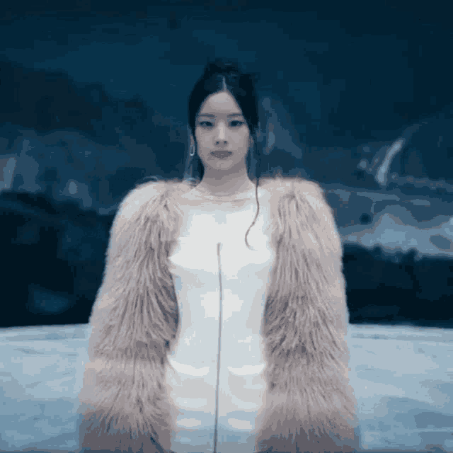 a woman in a white dress and a pink fur coat is standing in front of a dark background .