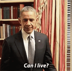 a man in a suit and tie is standing in front of a bookshelf and asking if he can live .