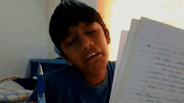 a young boy is looking at a notebook with a pen on his desk