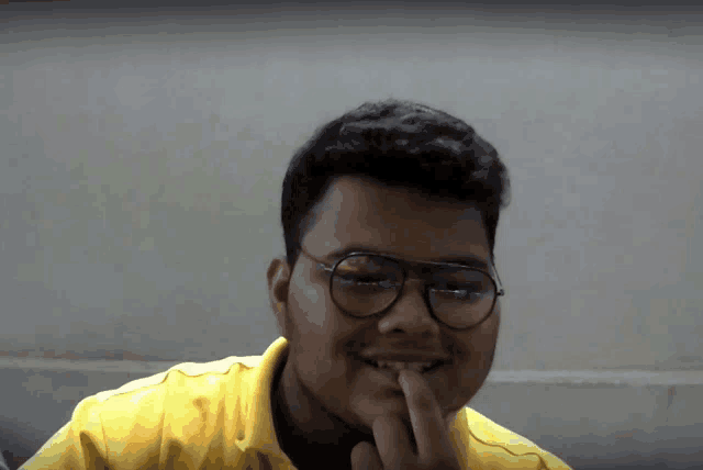 a young man wearing glasses and a yellow shirt smiles for the camera